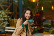 © olga pink - Portrait young Asian woman drinking coffee in cafe on terrace of cafe. Outdoors. Cozy autumn season