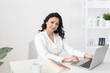 © satura_ - Indian woman beautician takes notes in office with laptop in cosmetology office with cosmetics background - cosmetologist business woman or doctor concept