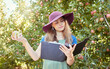 © J Maas/peopleimages.com - Research, farm and farmer reading about apple farming at an orchard for sustainability, agriculture and growth. Woman with fruit in the countryside for inspection, analysis and knowledge in nature