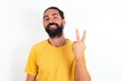 © Jihan - young bearded hispanic man wearing yellow T-shirt over white background smiling and looking friendly, showing number two or second with hand forward, counting down