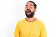 © Jihan - young bearded hispanic man wearing yellow T-shirt over white background yawns with opened mouth stands. Daily morning routine