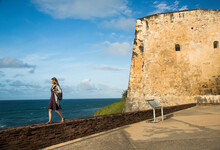 A Young Woman Walks On The Wall Of A Fortress In Old San Juan, Puerto Rico.