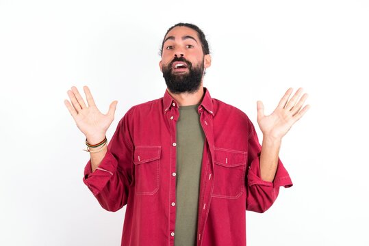 Surprised terrified Caucasian man with beard wearing red shirt Gestures with uncertainty, stares at camera, puzzled as doesn't know answer on tricky question, People, body language, emotions concept