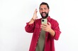 Angry Caucasian man with beard wearing red shirt over white background screaming on the phone, having an argument with an employee. Troubles at work.