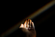 © Cavan Images - Unrecognizable female hand reaching out to a rainbow in the dark