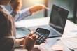 © Daenin - Young colleagues discuss business and analytical price charts using calculators and laptops to calculate financial, tax, accounting, statistics and analytical research ideas.