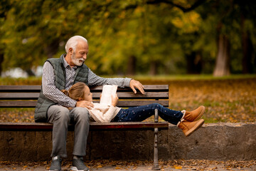 Wall Mural - Grandfather spending time with his granddaughter on bench in park on autumn day