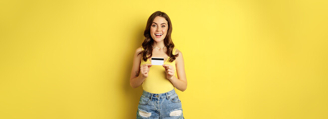 Wall Mural - Enthusiastic young woman showing credit card, recommending bank, discount in store, contactless payment or cashback, standing over yellow background