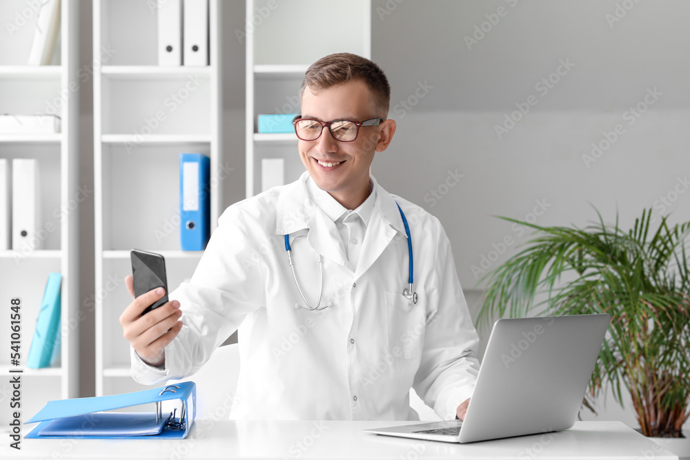 Male doctor with mobile phone taking selfie in clinic