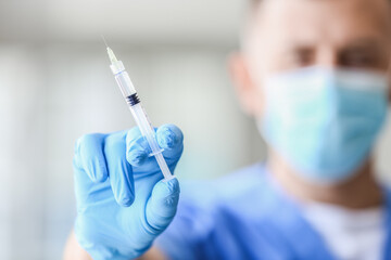 Wall Mural - Male doctor in medical mask with syringe at hospital, closeup