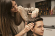 © velishchuk - Hair salon master does hair styling client at barber shop. Men's fashion and style. Hair care, beauty industry, barber concept. Barber shop men hairstyle. Young man getting a modern haircut