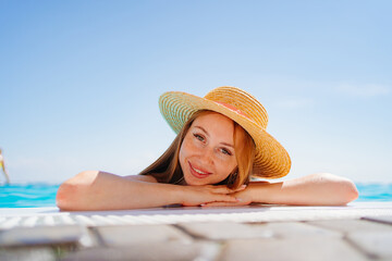 Wall Mural - portrait of a happy woman with eyes closed in a hat at the side of the pool