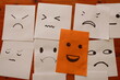 © CarlosJose - Papeles adhesivos en el tarjetero con caritas emotivas de enojo y sonriente de felicidad, muestran emociones de lo malo y lo bueno, formando un diseño original con fondo de la mesa de madera de cedro