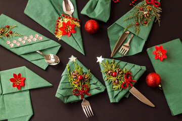 Wall Mural - Christmas green color,paper napkins folded in various shapes on black surface with cutlery set and christmas decoration.Top view