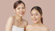 Close up portrait beauty shot of two young beautiful Asian girls looking at camera isolated on brown background.