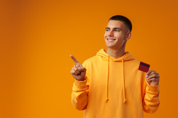 Sticker - Handsome young man holding credit card on yellow color background