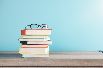 close up of stacked books and glasses on blurry blue background with mock up place. school and educa