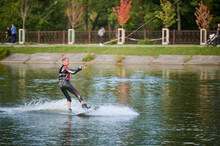 Wakeboarder Surfing On Lake. Young Man Surfer Having Fun Wakeboarding In The Cable Park. Water Sport, Outdoor Activity Concept.