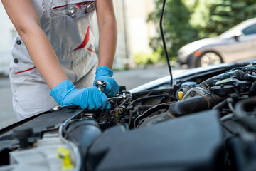 woman who works as a mechanic in a car service repairing the chassis of a car using a wrench.