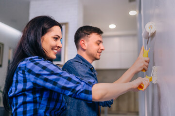 happy couple in shirt painting the walls of their new home with paint rollers.