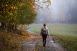 Woman hiking on footpath in autumn forest. Fog weather. Solo tourist