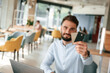 © standret - Holding credit cards. Young man is sitting in the cafe and working by using laptop