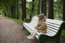 Adorable Little Girl Sitting On A Bench In Autumn Park On A Sunny Fall Day. Happy Child Having Fun Outdoors. Outdoor Autumn Activities For Kids