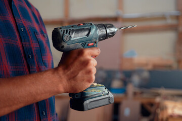 Close-up of mid adult man holding drill next to woodpile in woodworking factory