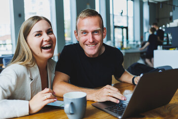 Wall Mural - Young colleagues managers are sitting at the table and laughing. Concept of business cooperation and teamwork. Young smiling people at the table in the office with a laptop. Modern successful people