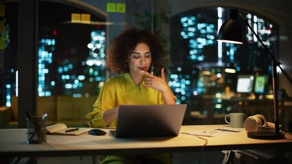 Portrait of a Happy Middle Eastern Manager Sitting at a Desk in Creative Office. Stylish Female with Curly Hair Using Laptop Computer, Thinking About a Business Strategy in Marketing Agency at Night.