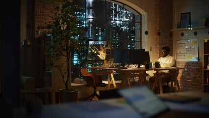 Aufkleber - Focused Project Manager Sitting at a Desk, Working Alone on a Computer in an Office at Night. African Marketing Specialist Researching a Project, Developing a Software Interface.