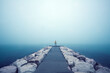 Eine Person mit Knalliger Kleidung steht am Ende Eines Weges der in das Meer ragt und von Wasser umgeben ist. Dichter See Nebel herrscht über dem Meer und macht eine Aussicht unmöglich.