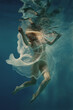 A woman with blond hair in a white dress swims underwater as if in weightlessness
