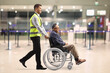 © Ljupco Smokovski - Full length profile shot of an airport worker pushing a mature man in a wheelchair at the airport