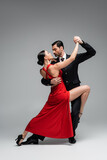Full length of elegant couple dancing tango on grey background