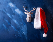 Traditional Symbols Of Christmas - Santa Claus Hat  And Deer On Dark Blue Murmur Background. Place For Text. Posrtcard.