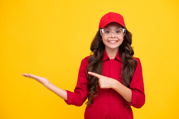 Wall Mural - Worker teenager child wearing overalls red, cap and protect glasses. Studio shot portrait isolated on yellow background. Pointing and showing concept.