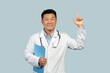 Cheerful middle aged chinese doctor in white coat with stethoscope showing finger up
