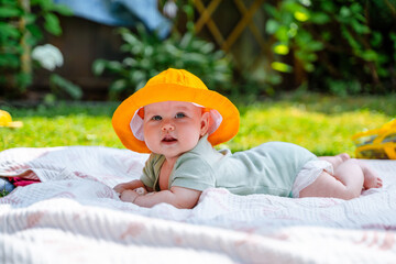 a cheerful kid little baby in a funny yellow panama lies on his tummy in nature on the grass