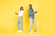 © Prostock-studio - Black Couple Using Phones Smiling To Each Other, Yellow Background
