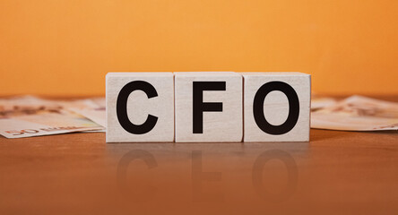 Wall Mural - CFO - an inscription on wooden cubes on an orange background along with banknotes. Finance and wear concept.