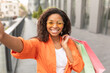 © Prostock-studio - Happy millennial african american lady in casual and glasses with many bags enjoys walk and takes selfie