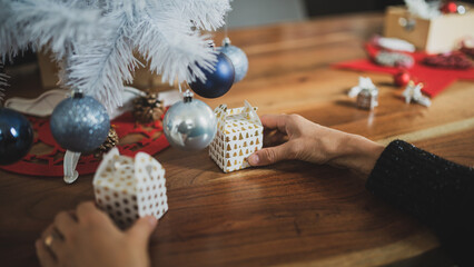 Closeup view of female hands preparing a holiday setting by placing small christmas gift boxes under a white tree