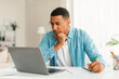 © Prostock-studio - Serious concentrated young black man in jeans looking at laptop, making notes, watching online lesson