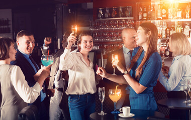 Wall Mural - Cheerful girls with coworkers funning in bar during firms party, dancing and toasting drinks