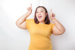 © Reezky - Excited Asian big sized woman wearing yellow shirt pointing at the copy space upside her, isolated by white background
