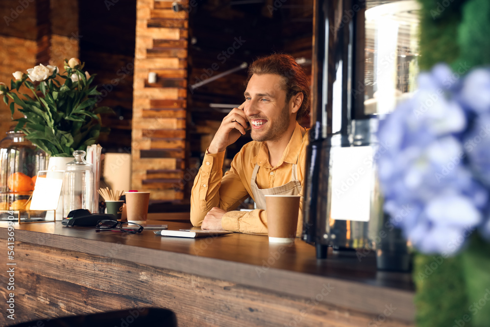 Young business owner talking by mobile phone at table in his cafe