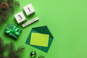 Cube calendar with date of DECEMBER 31, fir branches, gift box and blank card on green background