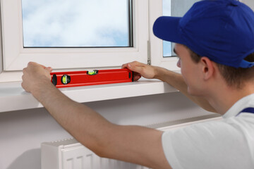 Poster - Worker using bubble level after plastic window installation indoors