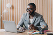 © VK Studio - Young smiling african american business in glasses sitting with coffee cup at workplace in office